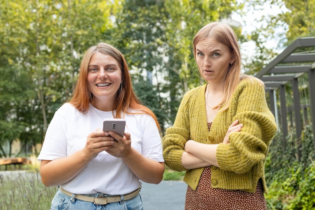 Zdjęcie szczęśliwa dziewczyna używa jej telefonu obsiadanie na ławce w parku sfrustrowana wzburzona dziewczyna siedzi obok fr