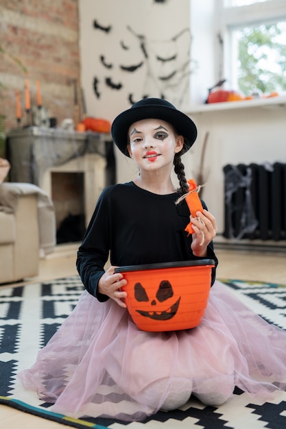 Szczęśliwa dziewczyna w halloweenowym stroju trzymająca kosz z smakołykami