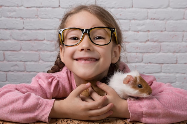Zdjęcie szczęśliwa dziewczyna w okularach, śmiejąca się, trzymająca w dłoniach świnkę morską, portret z bliska