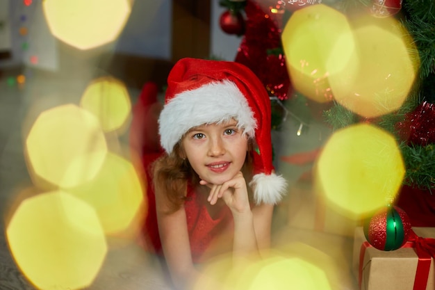 Szczęśliwa dziewczyna w Santa hat leżąca w pobliżu choinki w domu