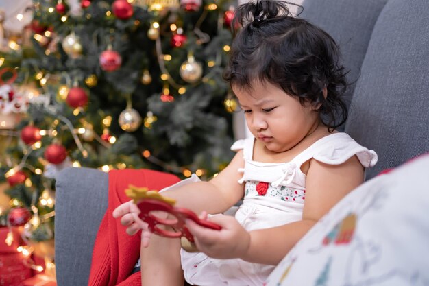 Szczęśliwa dziewczynka azjatyckich zabawy w Boże Narodzenie. Dziecko z rodzicem z dekoracją choinkową w domu na wakacjach.
