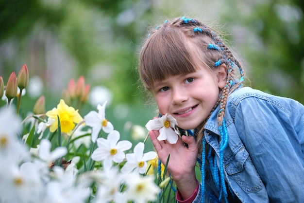 Szczęśliwa dziewczynka bawi się w letnim ogrodzie, ciesząc się słodkim zapachem białych kwiatów narcyzów w słoneczny dzień