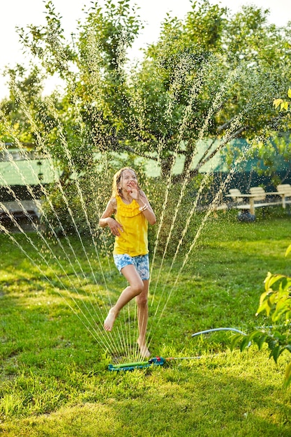 Szczęśliwa dziewczynka bawiąca się zraszaczem ogrodowym biega i skacze latem