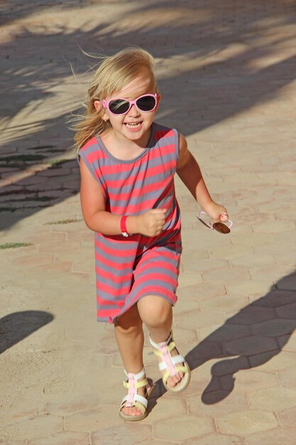 Zdjęcie szczęśliwa dziewczynka biegająca w parku miejskim pozytywne dziecięce emocje dziecko biegające ścieżką uśmiechnięte i radujące się szczęśliwe dzieciństwo