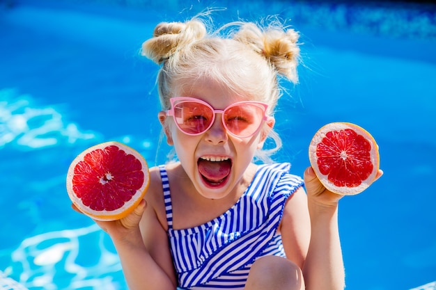 szczęśliwa dziewczynka jedzenie owoców latem przy basenie