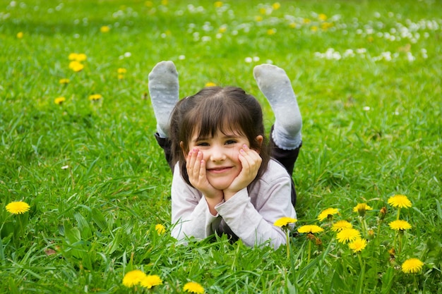 Szczęśliwa dziewczynka leżąca na trawie z rękami trzymającymi twarz i stopy w parku