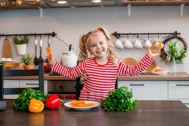 Szczęśliwa dziewczynka przygotowuje sałatkę z warzyw w kuchni
