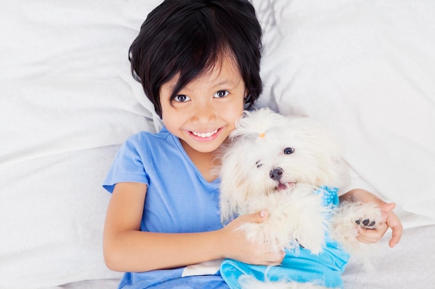 Szczęśliwa dziewczynka przytulająca maltańskiego psa na łóżku