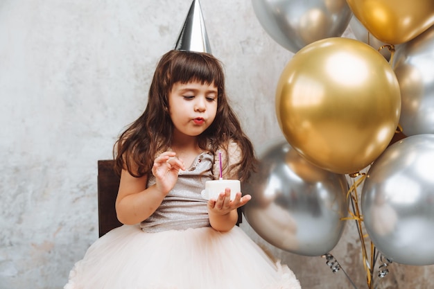 Szczęśliwa dziewczynka składa życzenie i zdmuchuje świeczki na balonach na ciasto Miejsce na tekst ozdobna ściana urodzinowa