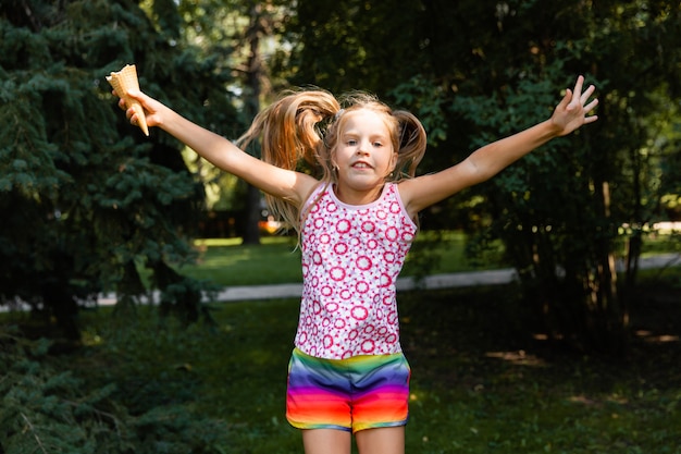Szczęśliwa dziewczynka skoki w parku. mała dziewczynka jedzenie lodów i zabawy w mieście.