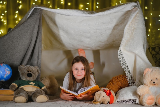Szczęśliwa dziewczynka śmiejąca się i czytająca książkę w ciemności w namiocie w domu
