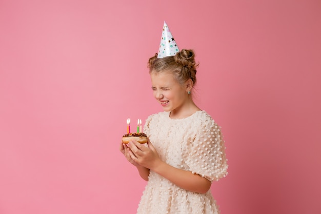 Szczęśliwa dziewczynka w czapce na urodziny składa życzenie i zdmuchuje świeczki na torcie.
