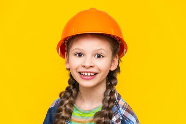 Szczęśliwa dziewczynka w kasku budowlanym i koszuli na żółtym, izolowanym tle Dziecko przygotowuje się do naprawy w przedszkolu Zawód inżyniera Żółte, izolowane tło