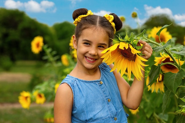 Szczęśliwa dziewczynka w niebieskiej sukience stoi obok kwiatów ozdobnego słonecznika