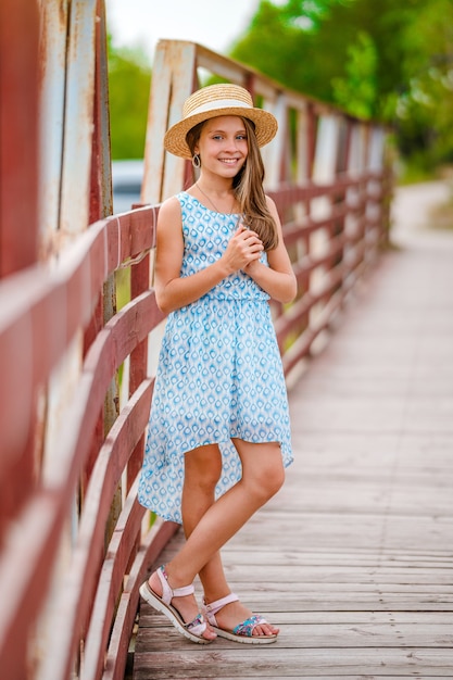 Szczęśliwa dziewczynka w niebieskiej sukience w letnim ogrodzie z drewnianym mostkiem