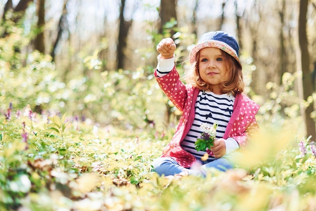 Szczęśliwa dziewczynka w niebieskim kapeluszu spaceruje po wiosennym lesie w ciągu dnia