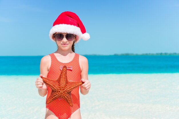 Szczęśliwa dziewczynka w Santa hat podczas świątecznych wakacji na plaży ma dużo zabawy