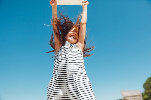 Szczęśliwa dziewczynka w słomkowym kapeluszu skacząca na plaży w letnie wakacje