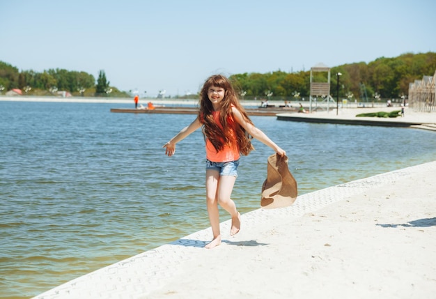 Szczęśliwa dziewczynka z długimi włosami biega wzdłuż plaży