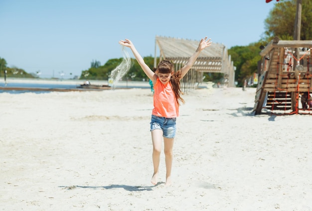 Szczęśliwa dziewczynka z długimi włosami biega wzdłuż plaży
