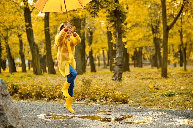 Zdjęcie szczęśliwa dziewczynka z parasolką i kaloszami skaczącymi w kałuży na jesiennym spacerze