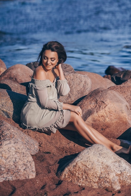 Szczęśliwa elegancka uśmiechnięta młoda kobieta pozuje na plaży