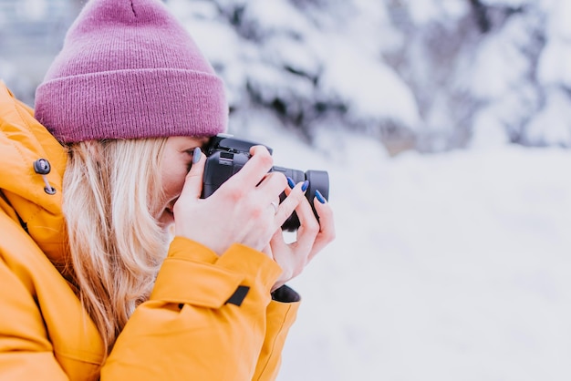 Szczęśliwa fotografka w żółtej kurtce robi zdjęcia zimy w zaśnieżonym parku