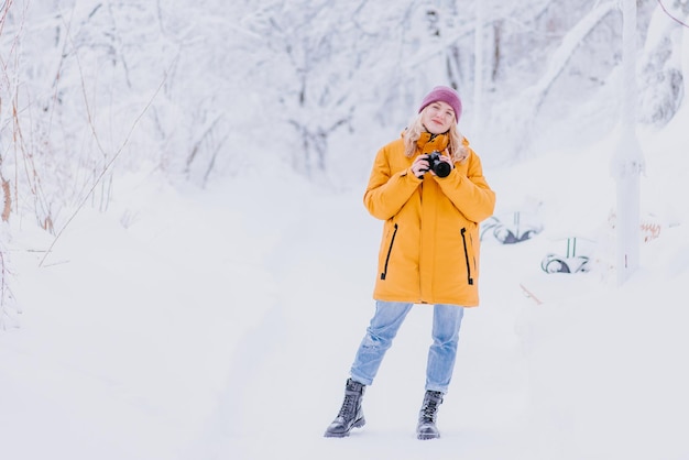 Szczęśliwa fotografka w żółtej kurtce robi zdjęcia zimy w zaśnieżonym parku