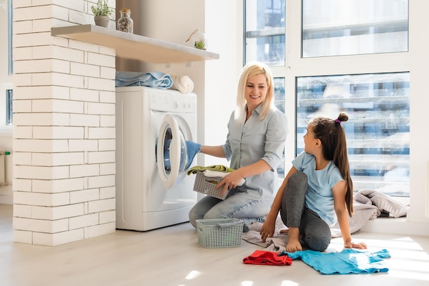 Szczęśliwa gospodyni domowa i jej córka z pościelą w pobliżu pralki