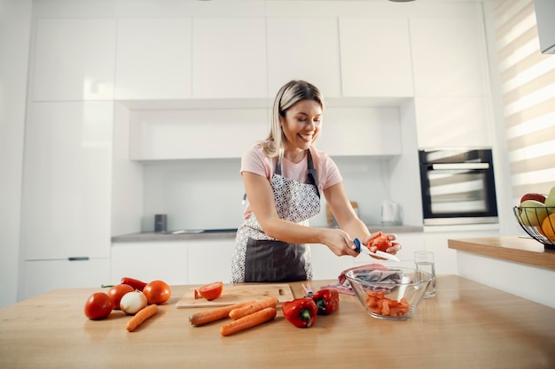 Szczęśliwa gospodyni domowa tnie pomidory na sałatkę w swojej nowoczesnej kuchni