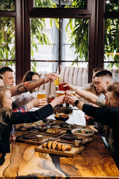 Szczęśliwa grupa przyjaciół pijących i klinkających z piwem i koktajlami w restauracji Brewery Bar Beverage lifestyle concept z chłopcami i dziewczynami bawiącymi się razem