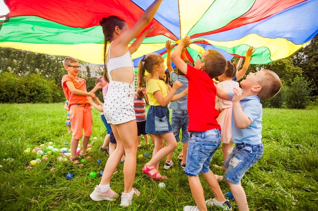 Zdjęcie szczęśliwa grupa skacząca pod dużym kolorowym baldachimem próbująca go dotknąć gry sportowe na świeżym powietrzu dla dzieci w różnym wieku osiągnięcie koncepcji radości i szczęścia