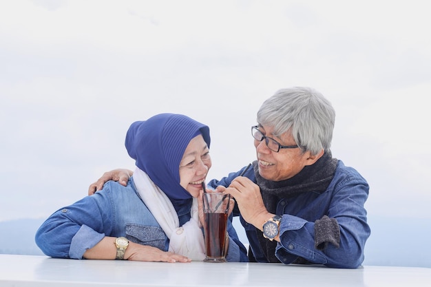 Szczęśliwa i zdrowa starsza para siedzi i pije herbatę razem w jednej szklance Niekończąca się miłość