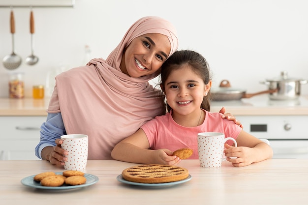 Szczęśliwa islamska rodzina mama i mała córka jedzą razem przekąski w kuchni