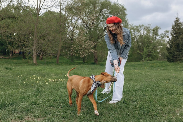 Szczęśliwa kobieta bawiąca się z aktywnym psem Rhodesian Ridgeback kijem podczas zabawy w parku