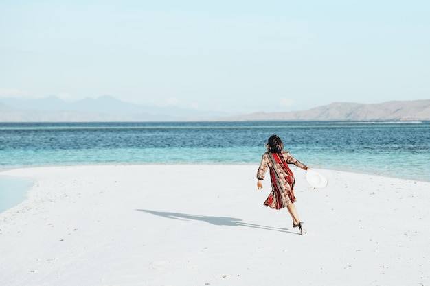 Szczęśliwa kobieta biegająca i tańcząca na białej, piaszczystej plaży