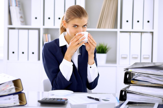 Szczęśliwa kobieta biznesu lub księgowa mająca kilka minut na kawę i przyjemność w miejscu pracy