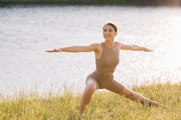 Szczęśliwa kobieta ćwiczy jogę na świeżym powietrzu nad rzeką
