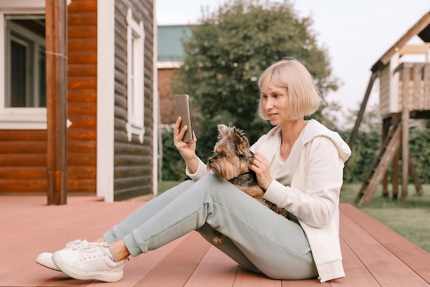 Szczęśliwa kobieta i pies yorkshire terrier podczas zabawy robią sobie portret selfie na smartfonie