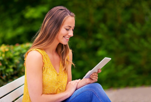 Szczęśliwa kobieta i tablet w parku do czytania badań i tworzenia sieci dla projektu szkolnego Uśmiech studenta college'u i technologia na ławce lub na kampusie do komunikacji w mediach społecznościowych i online lub ebook