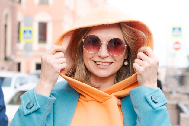 Szczęśliwa kobieta idzie przez miasto z torbą w ręku ubrana w jasne ubrania pomarańczowy kaptur i
