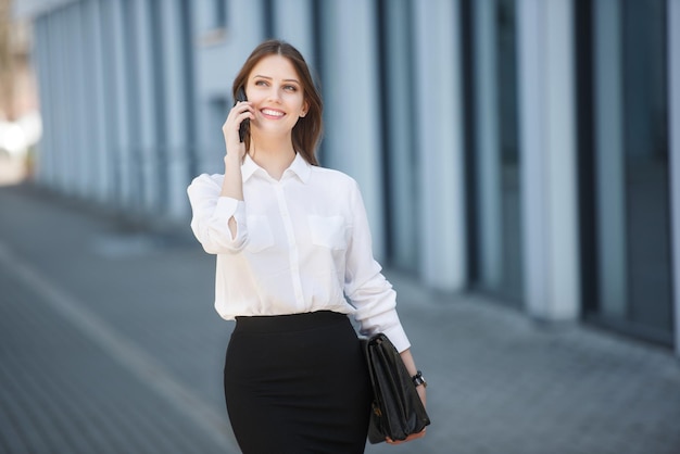 Szczęśliwa kobieta idzie ulicą i rozmawia przez telefon komórkowy