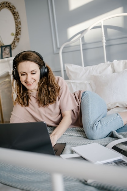 Szczęśliwa kobieta na co dzień ze słuchawkami, pracująca na laptopie zdalnie z domu