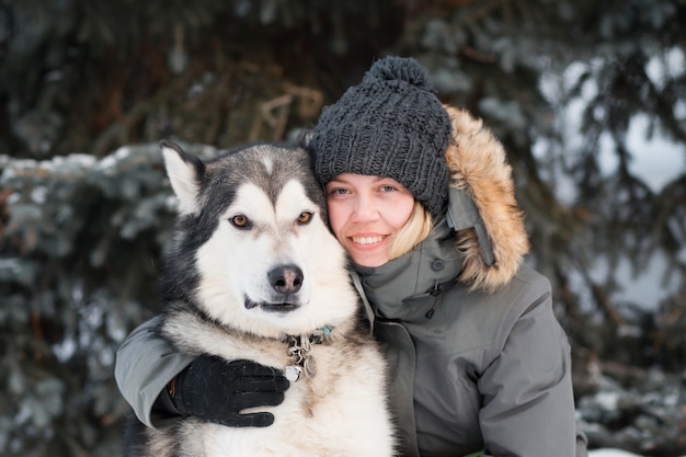 Szczęśliwa kobieta obejmując alaskan malamute w zimowym lesie. ścieśniać.