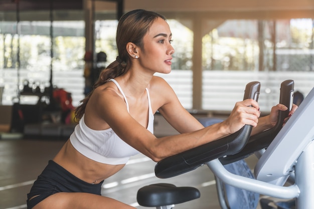 Szczęśliwa Kobieta Ono Uśmiecha Się Podczas ćwiczyć Na Rower Maszynie Przy Gym Sporta Klubem.