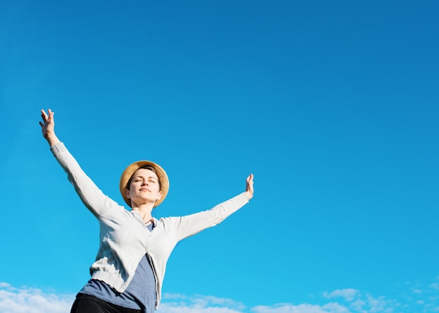 Szczęśliwa kobieta podnosi jej ręki wysoko przeciw niebieskiemu niebu