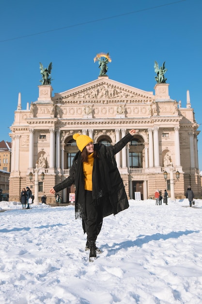 Szczęśliwa kobieta podróżnik przed budynkiem opery we lwowie w sezonie zimowym zaśnieżone miasto