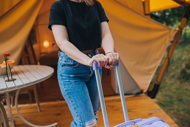 Szczęśliwa kobieta podróżnik z bagażem stojącym na tle przytulnego glampingowego domu Luksusowy namiot kempingowy na zewnątrz letnie wakacje i wakacje Koncepcja stylu życia