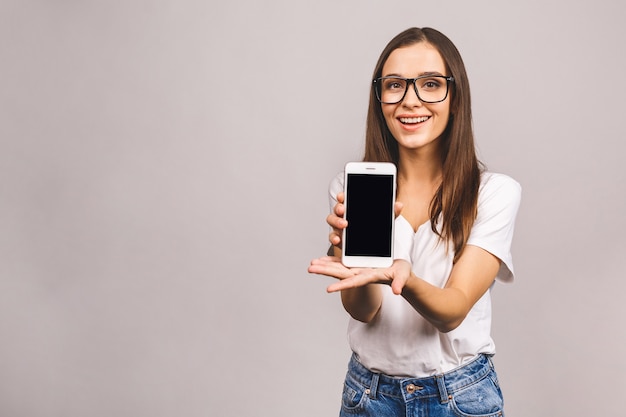 Szczęśliwa kobieta pokazuje pusty ekran smartfona, patrząc w kamerę z otwartymi ustami