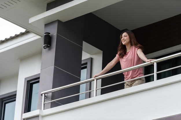 Szczęśliwa kobieta relaksująca się i patrząca z balkonu swojego domu